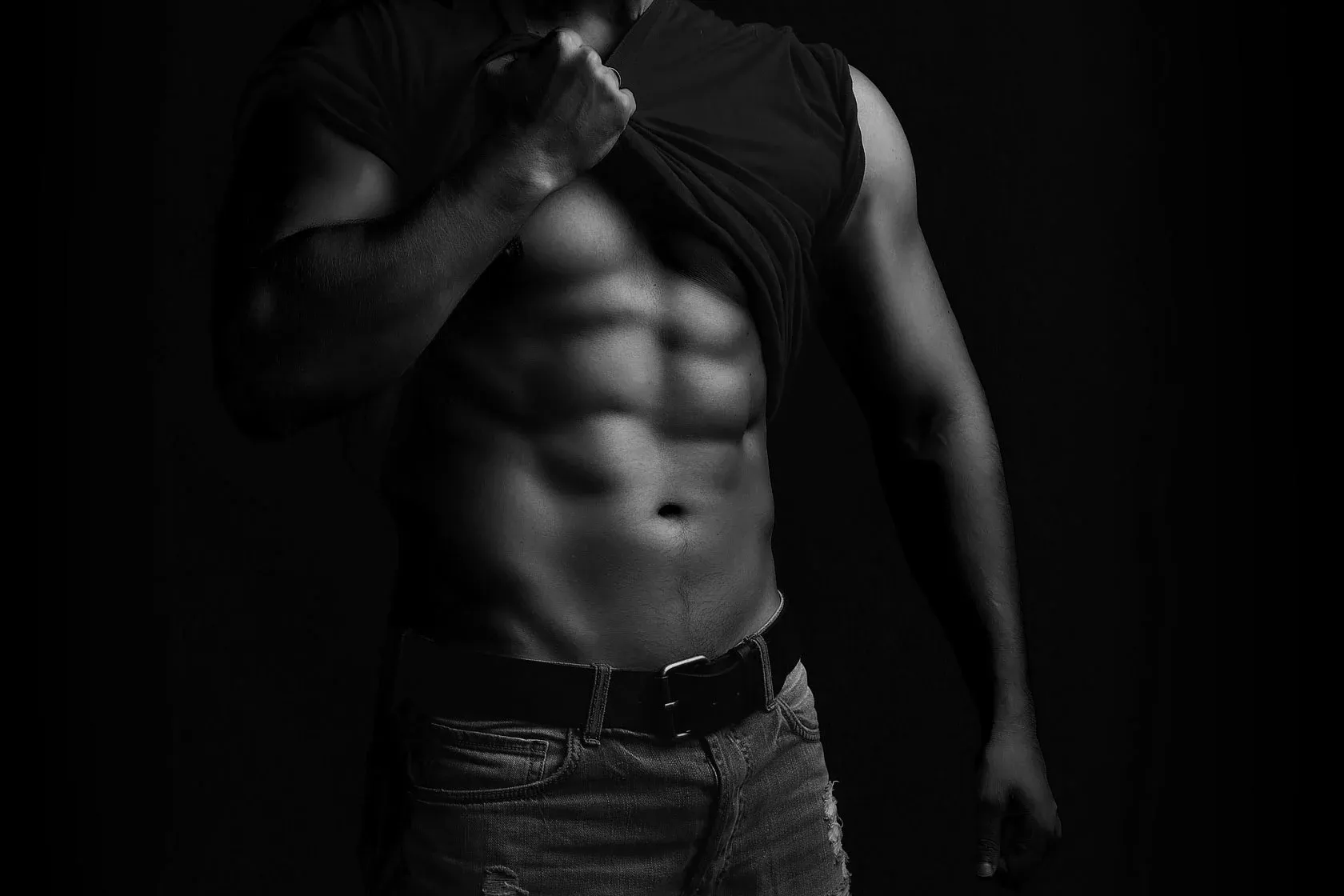Man showcasing fit abs in low-light setting.