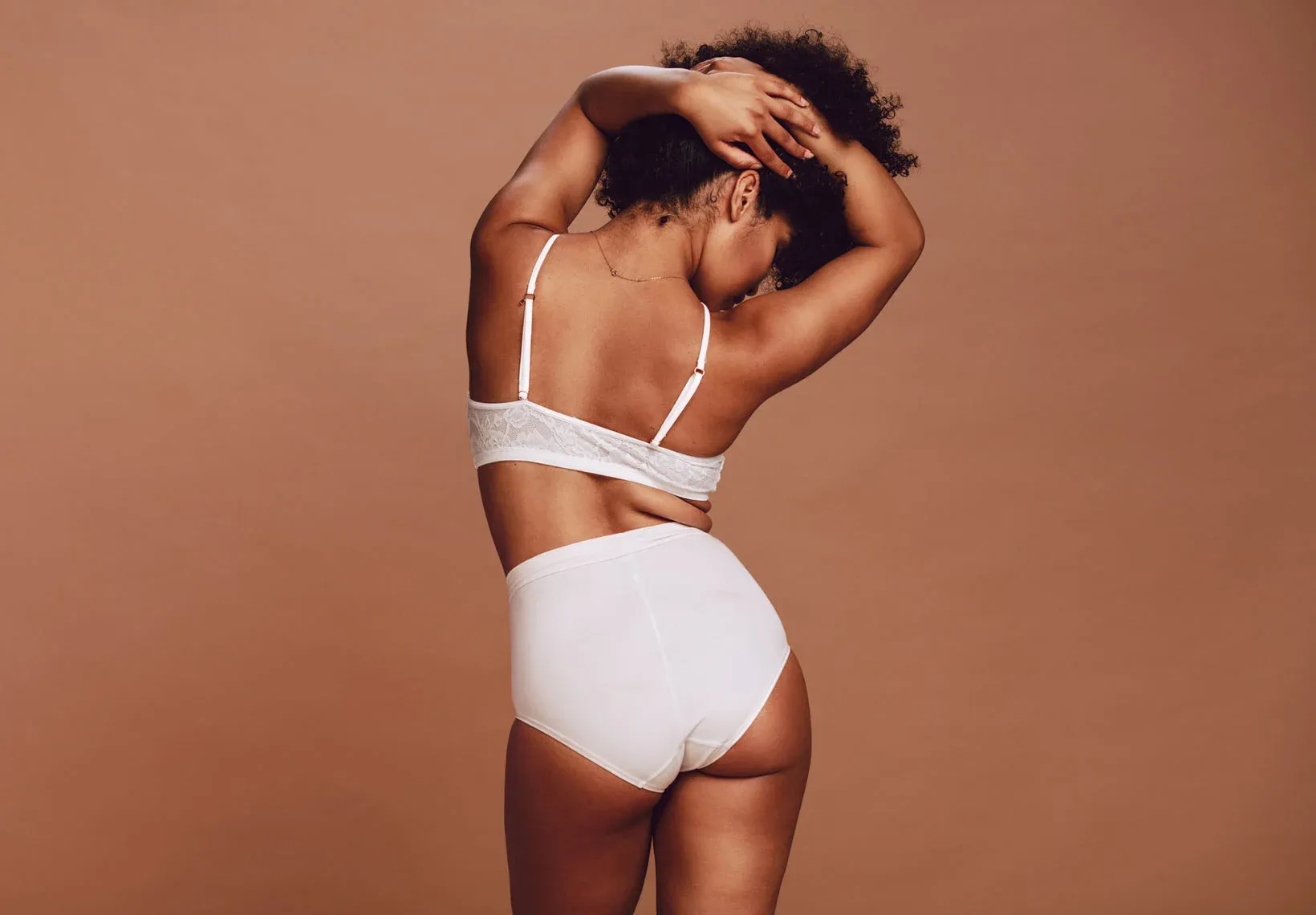 Woman posing in white underwear, back view.