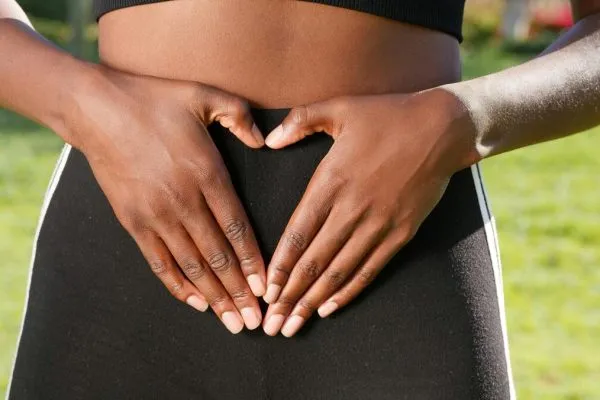 A woman making a heart shape with her hands on her belly