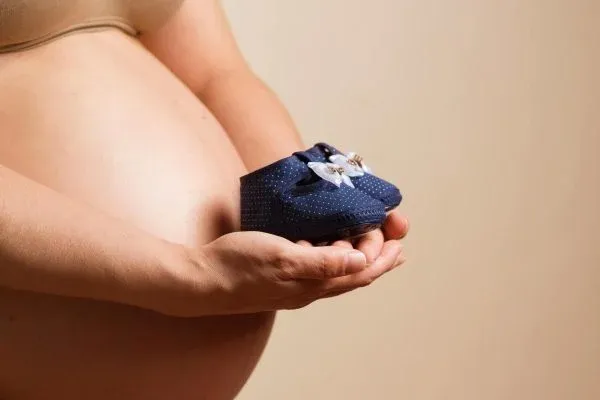 A pregnant woman holding her baby's shoes